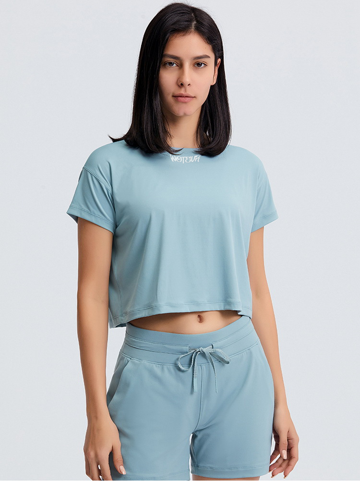 Woman wearing a light blue crop top and shorts set on a white background